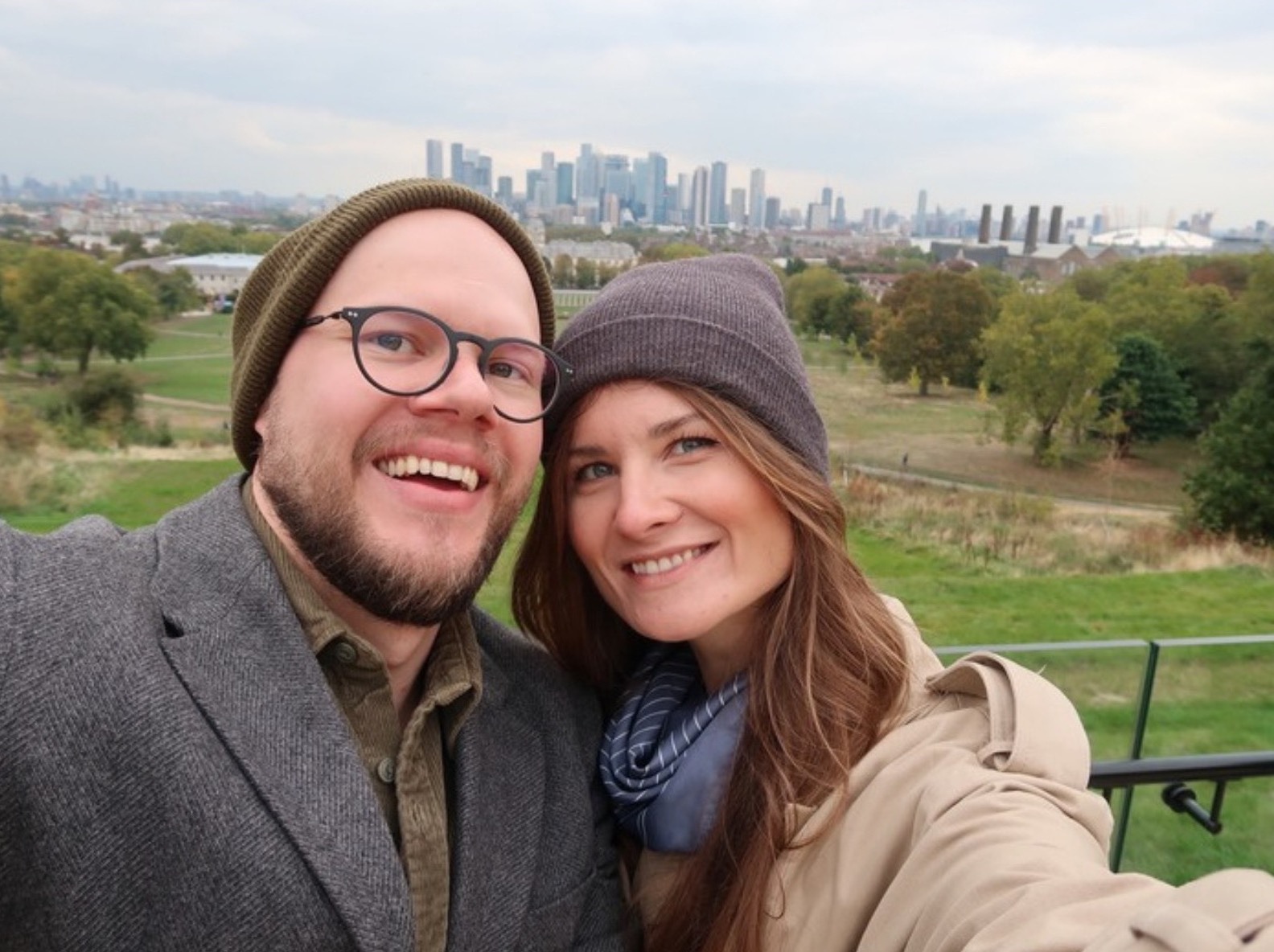 Karolina i Krzysztof w czapkach i płaszczach, uśmiechnięci na tle panoramy miasta